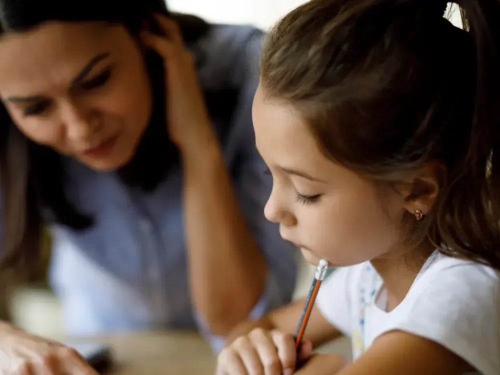 A parent helping her daughter with homework at the kitchen table