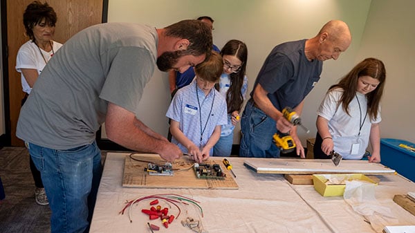 Two men give a boy and girl student a maintenance repair demonstration