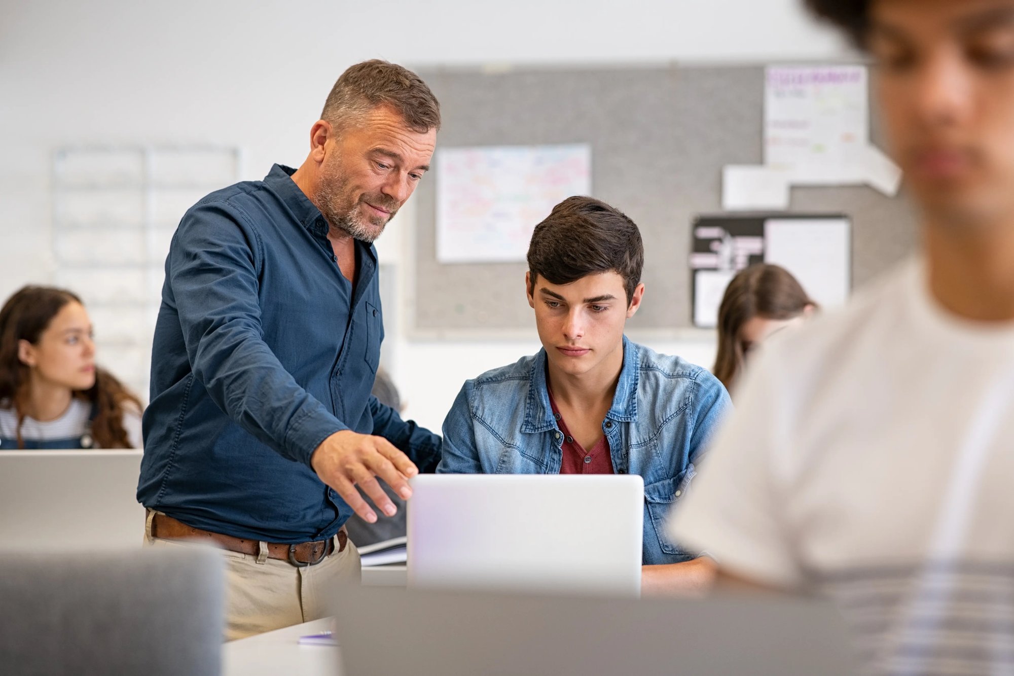 male teacher helping student at laptop
