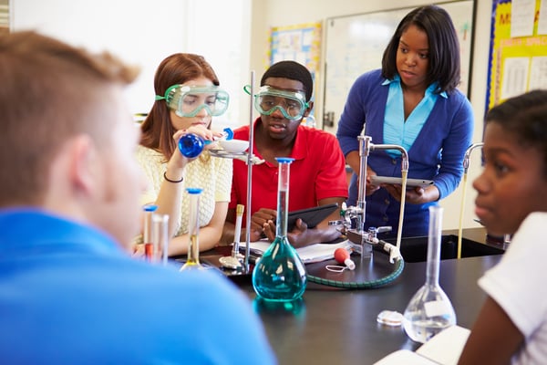 diverse group of students doing a science experiment while a teacher watches