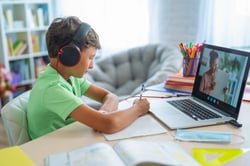 young boy doing homework while watching a laptop